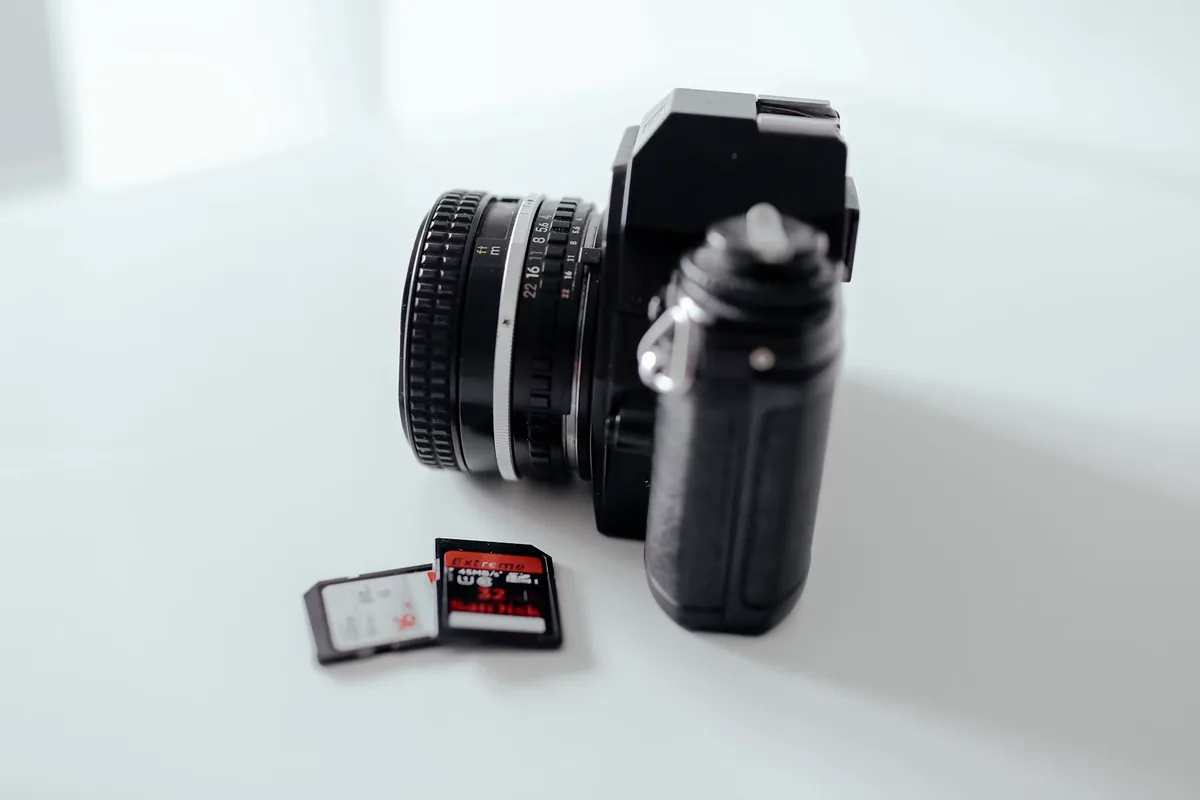 Two SD memory cards beside a camera on a pale tabletop