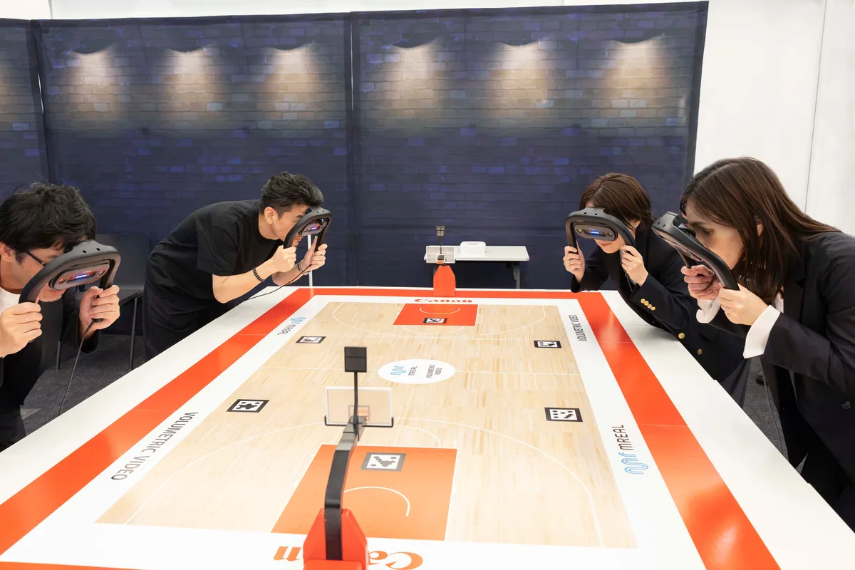 Four participants holding Canon mixed-reality viewers around a tabletop basketball court at the demonstration.