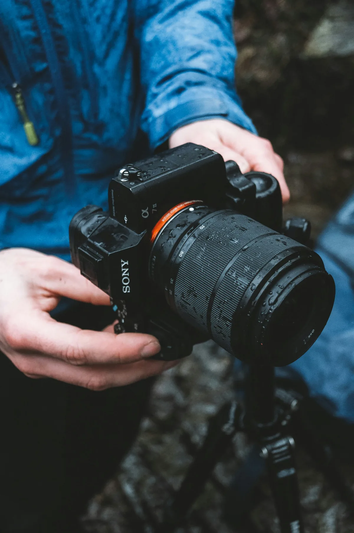 Hands holding a Sony camera with water droplets on its surface.