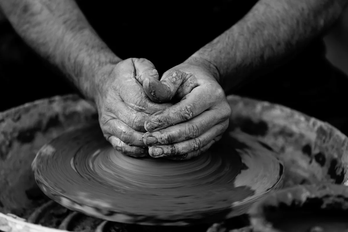 Black-and-white close-up of hands shaping clay on a pottery wheel.