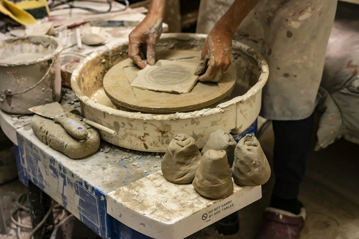 Potter working with clay at a wheel beside studio tools.