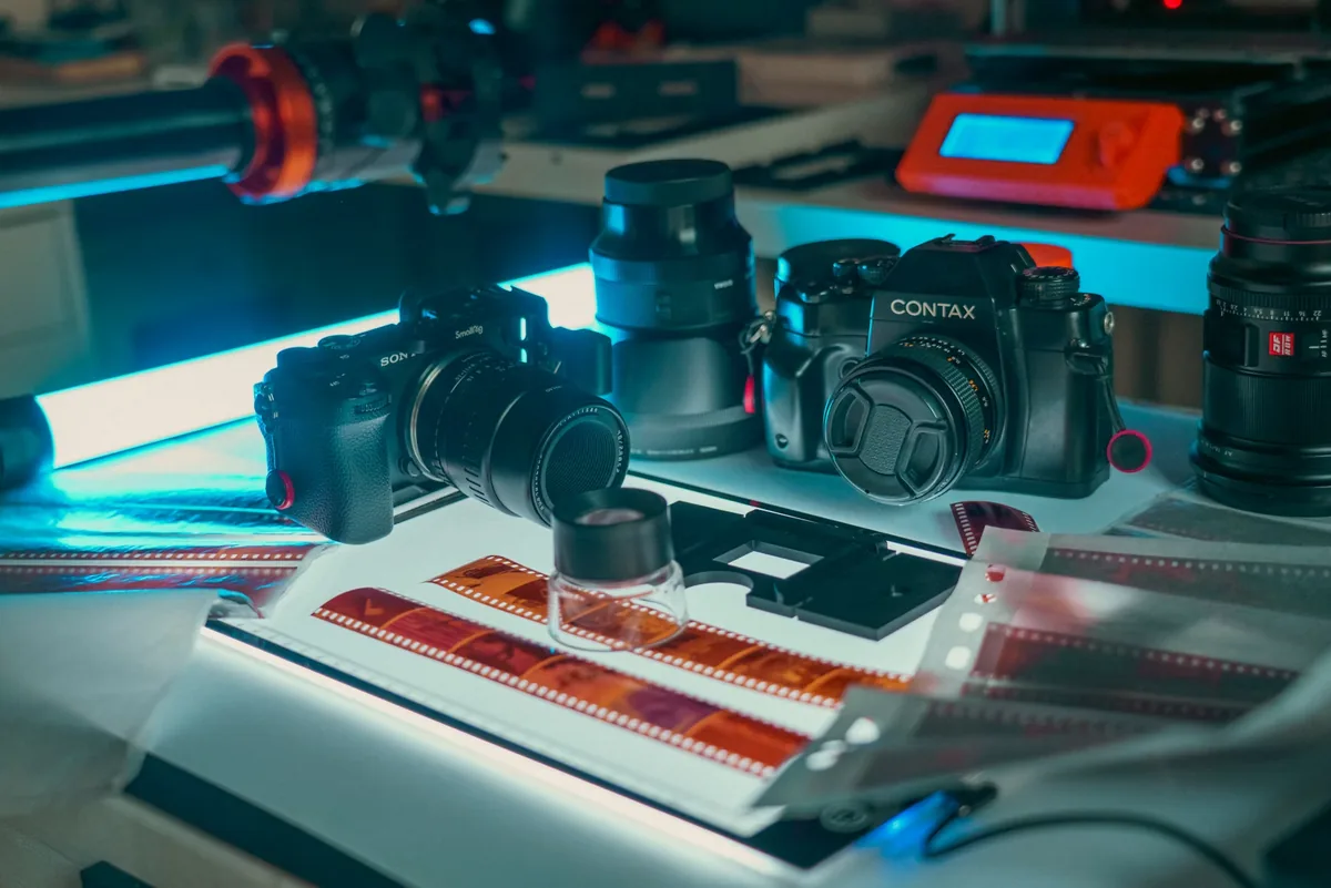 Cameras, a film scanner and strips of photographic negatives arranged on a desk