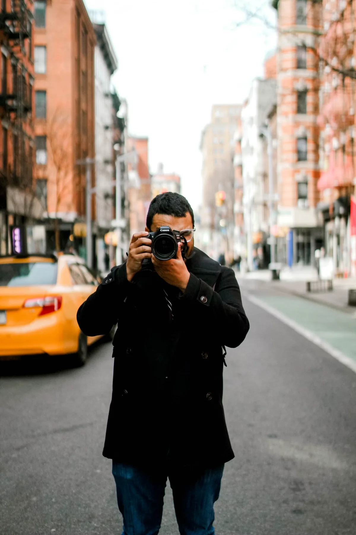 A photographer standing in a city street with a camera raised to their face