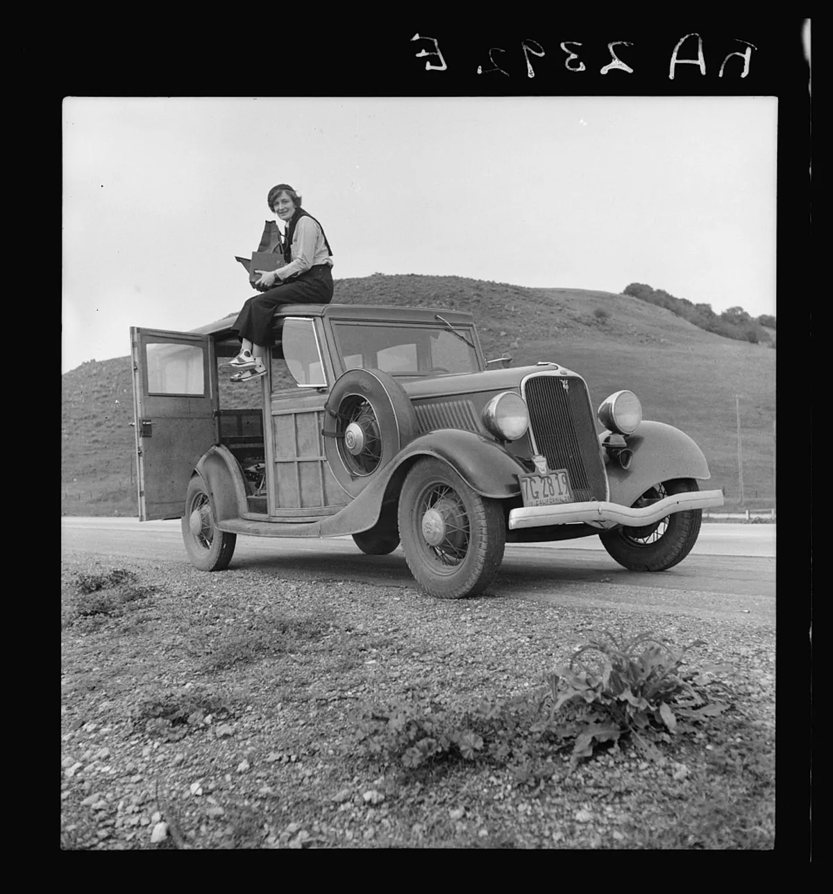 Dorothea Lange seated on the roof of a station wagon while working in California in 1936