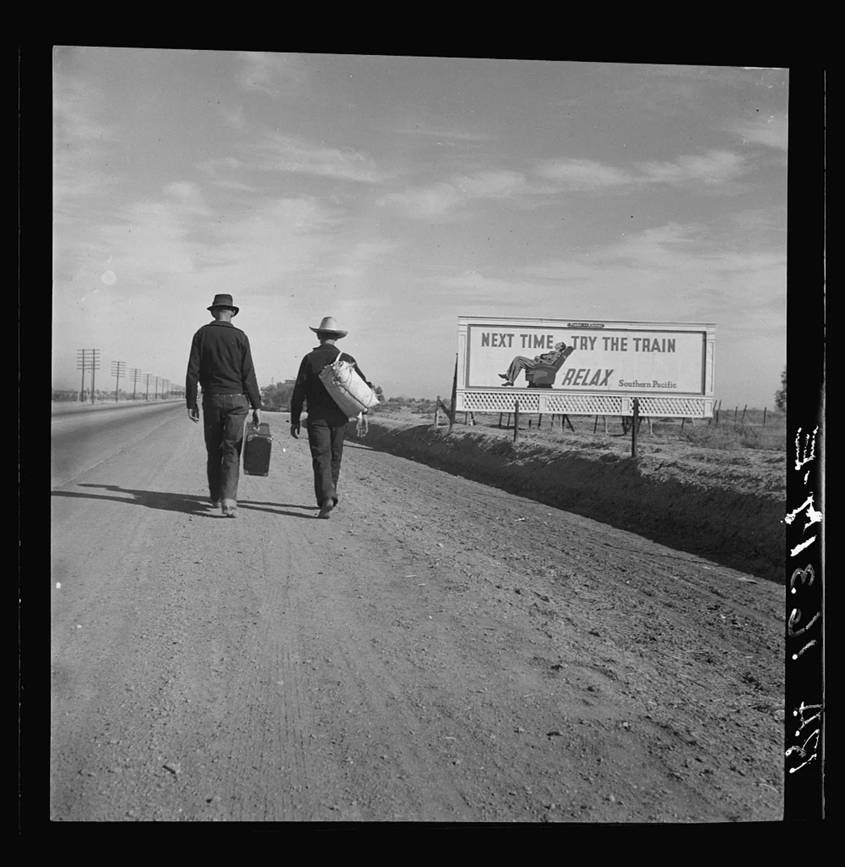 Two migrant travelers walking beside a California road toward Los Angeles in 1937