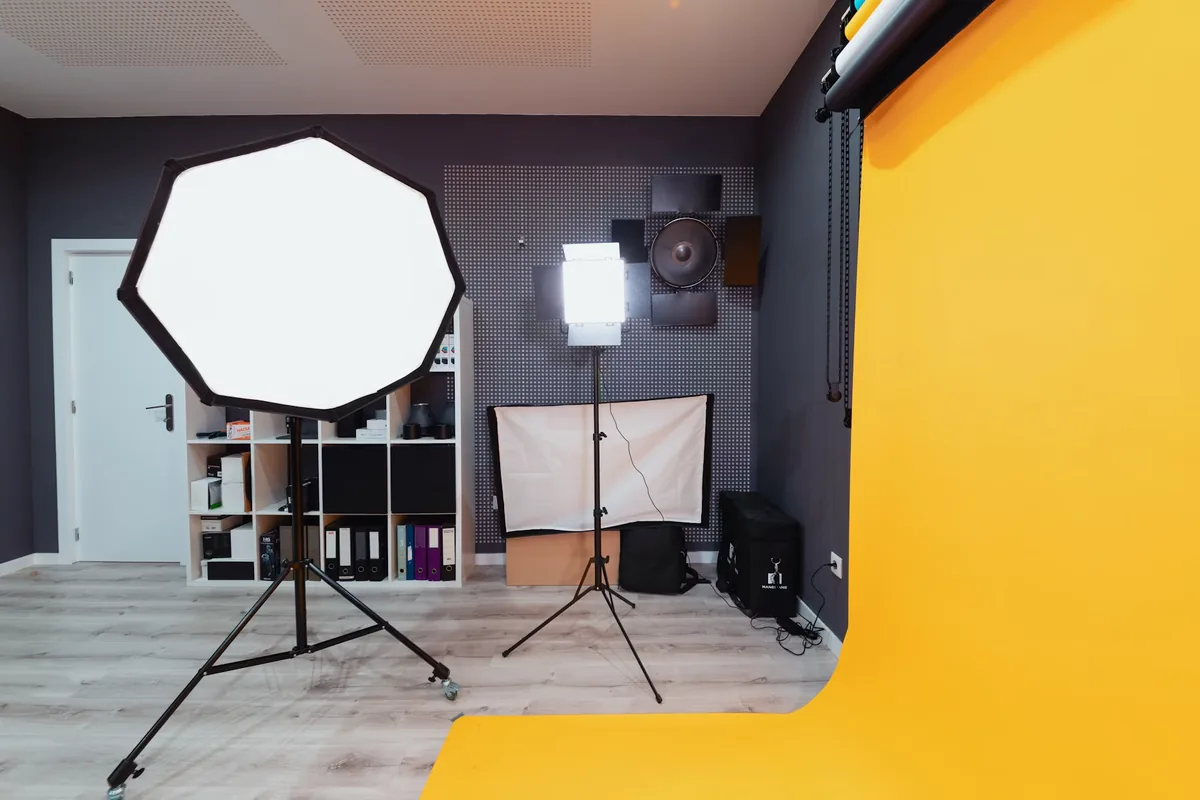An illuminated octagonal softbox and rectangular panel light beside a yellow studio backdrop