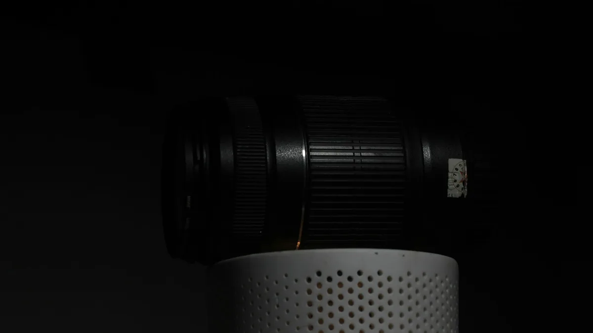 Camera lens lying horizontally on a perforated white stand against a dark background.