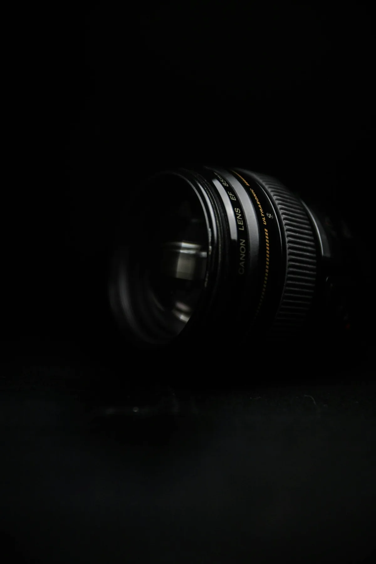 Canon EF 85mm lens standing on a dark surface with its front glass angled toward the viewer.