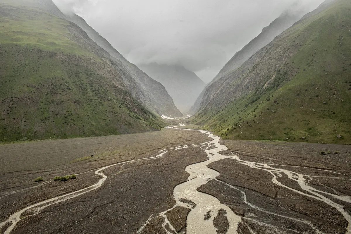 Branching streams running along a broad valley between steep green mountain slopes.