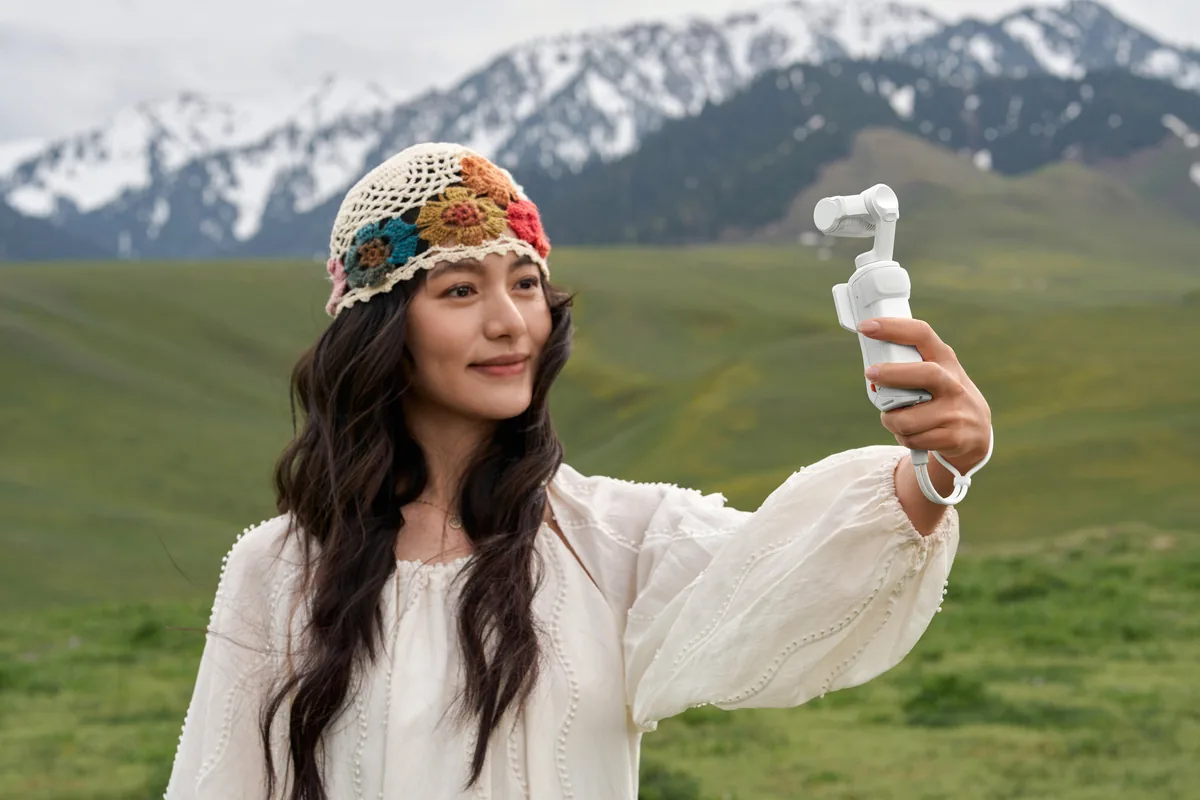 Woman holding a white Insta360 Luna Ultra in a mountain landscape.
