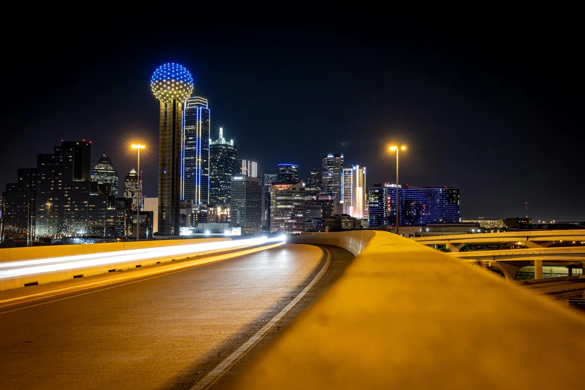 Night skyline with curved vehicle light trails, illustrating fixed architecture and moving subjects.
