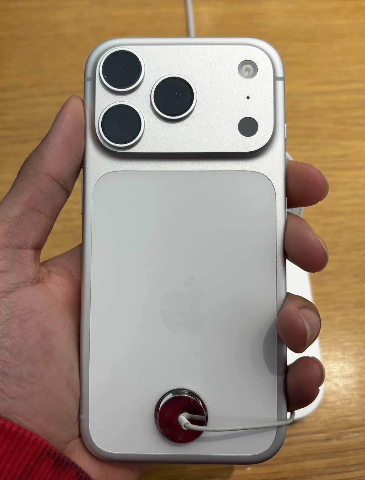 Hand holding the back of a silver iPhone 17 Pro attached to a store security cable.