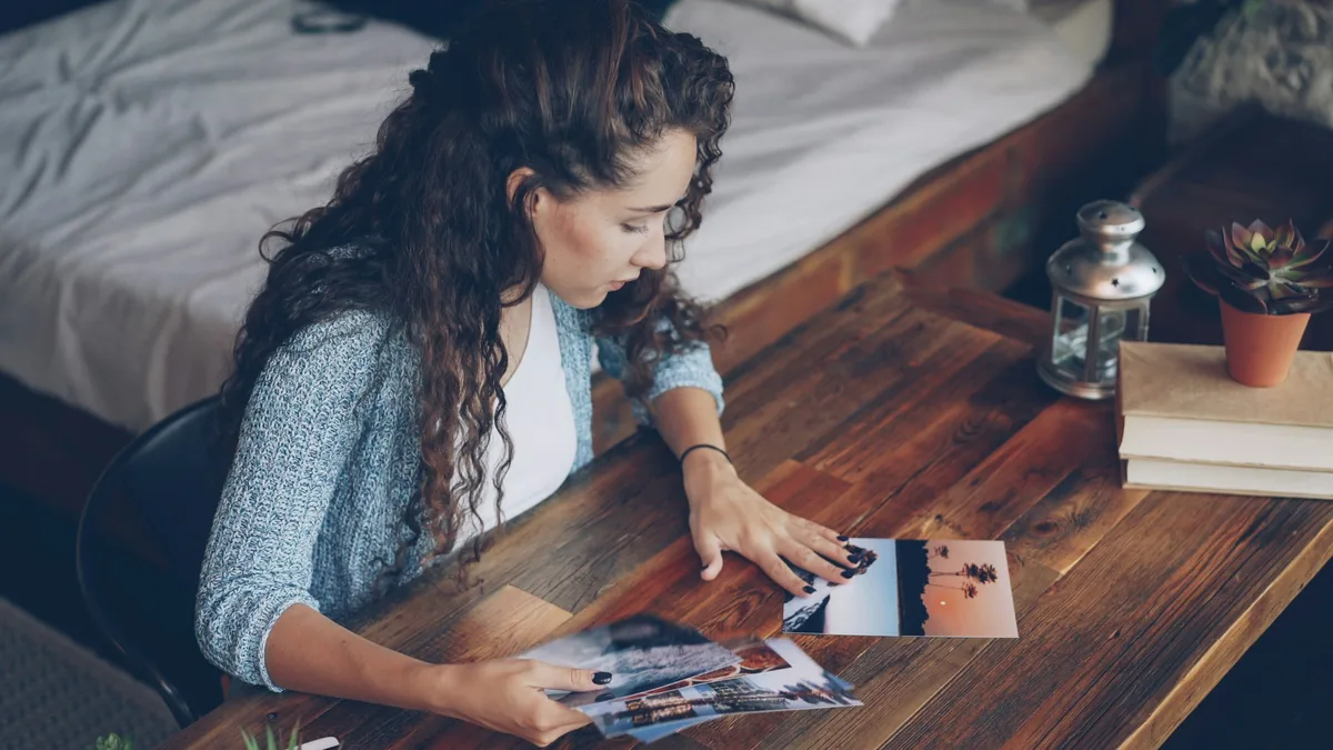 Woman examining photographic prints on a wooden table.
