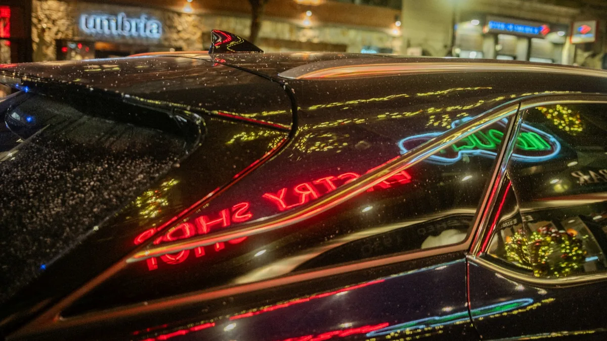 Red and green illuminated signs reflected in the rain-covered windows and roof of a parked car.