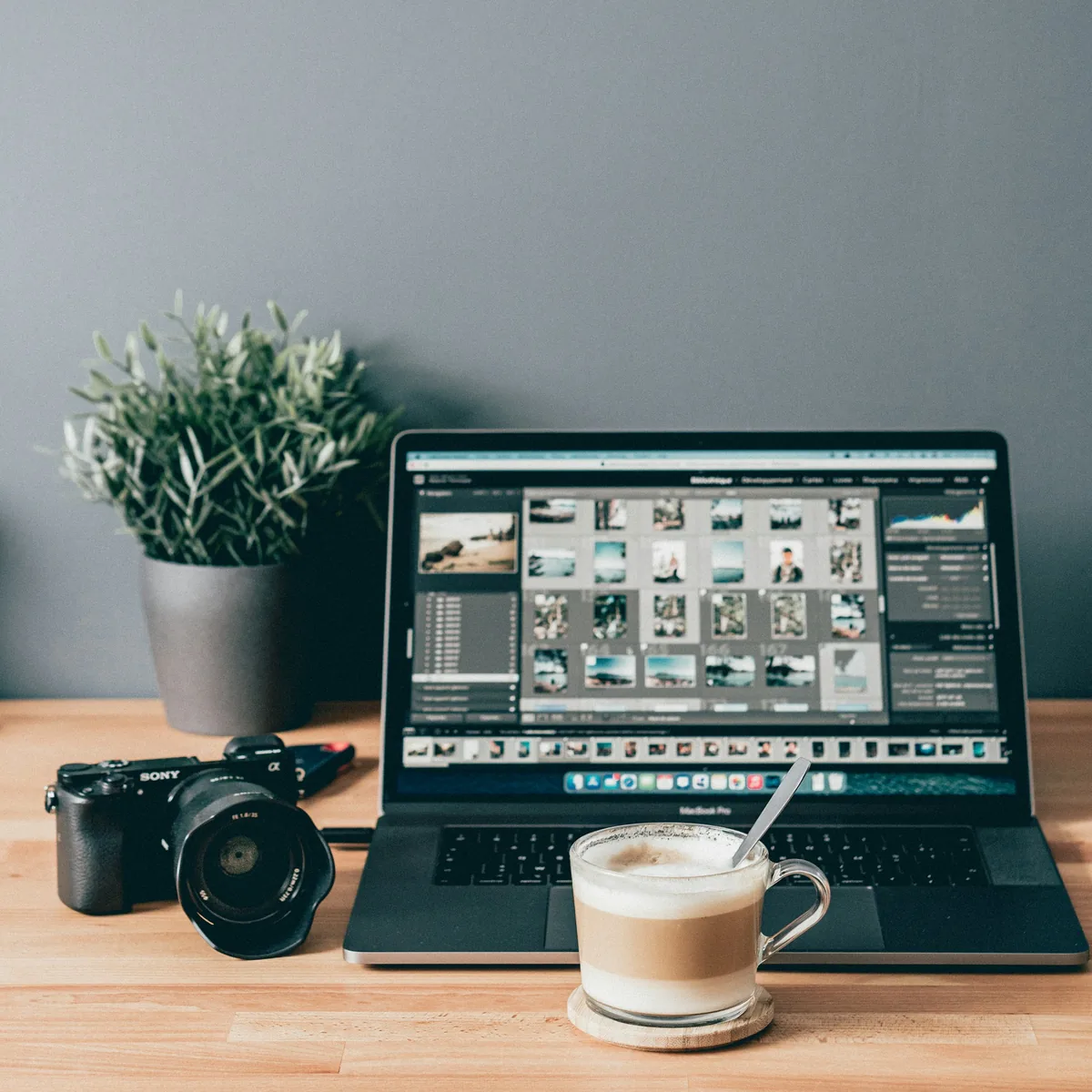 Laptop displaying a photo library beside a camera and coffee.