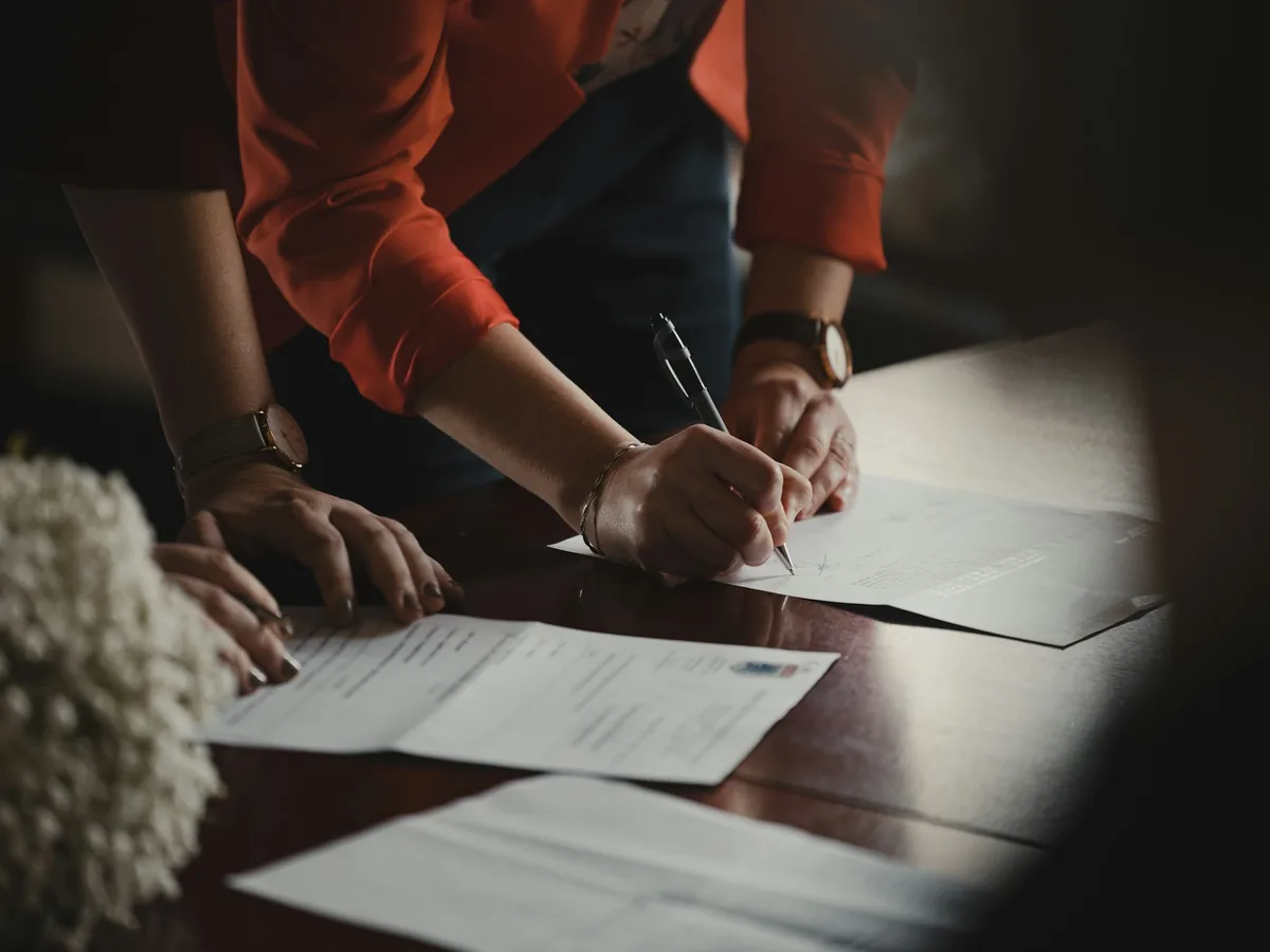 Hands writing on paperwork at a table.