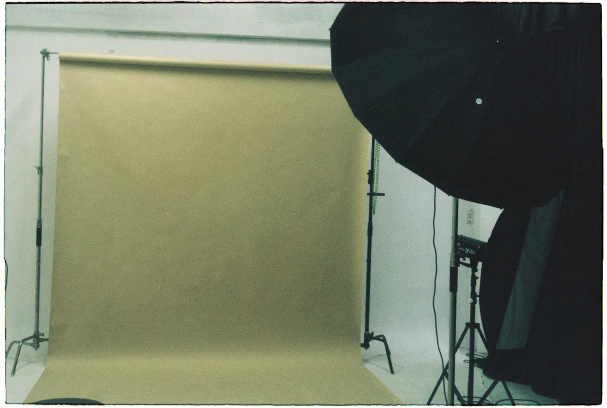 Empty photographic studio with a tan paper sweep, black lighting umbrella and stands.