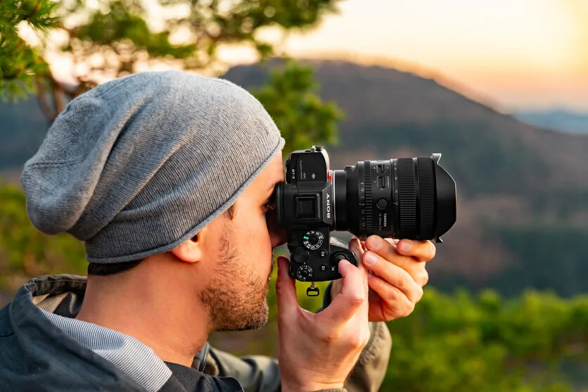 A photographer using a mirrorless camera and zoom lens outdoors