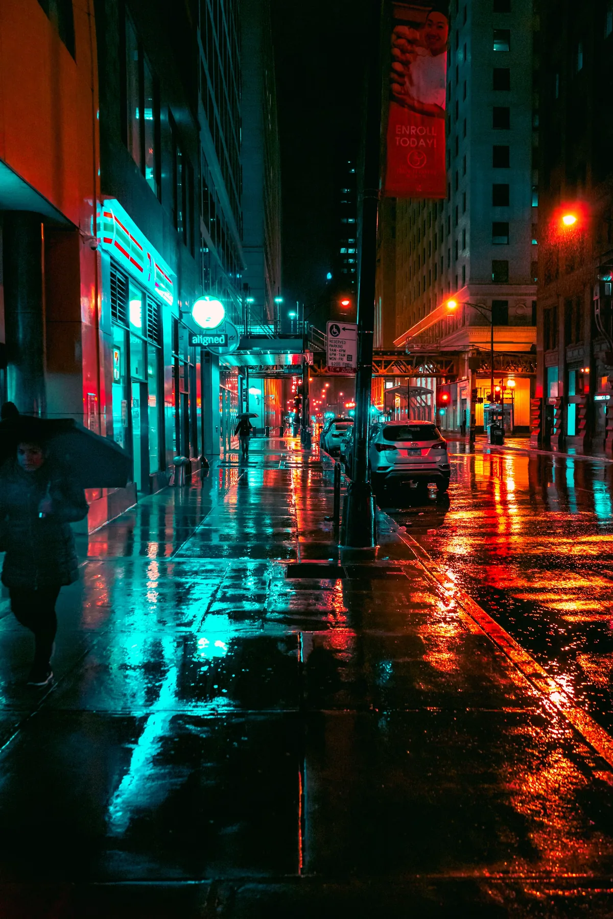 A lone figure with an umbrella walking through a rain-lit street