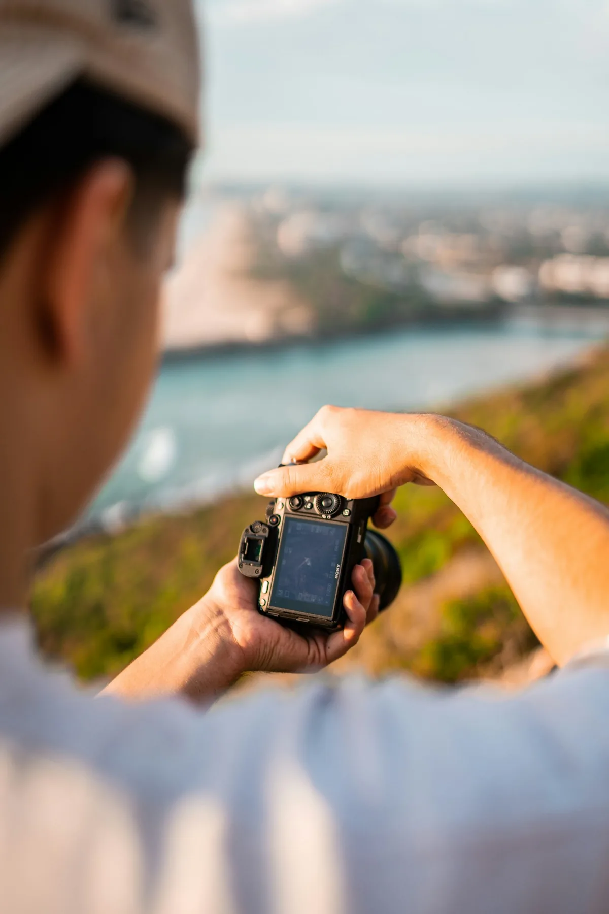 A person holding a Sony camera with its rear screen and controls visible above a coastal background