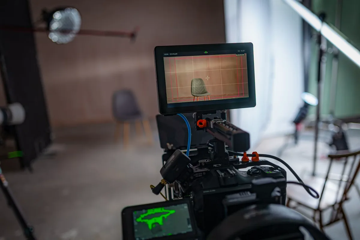 Video camera and external monitor framing a chair on a lit interview set