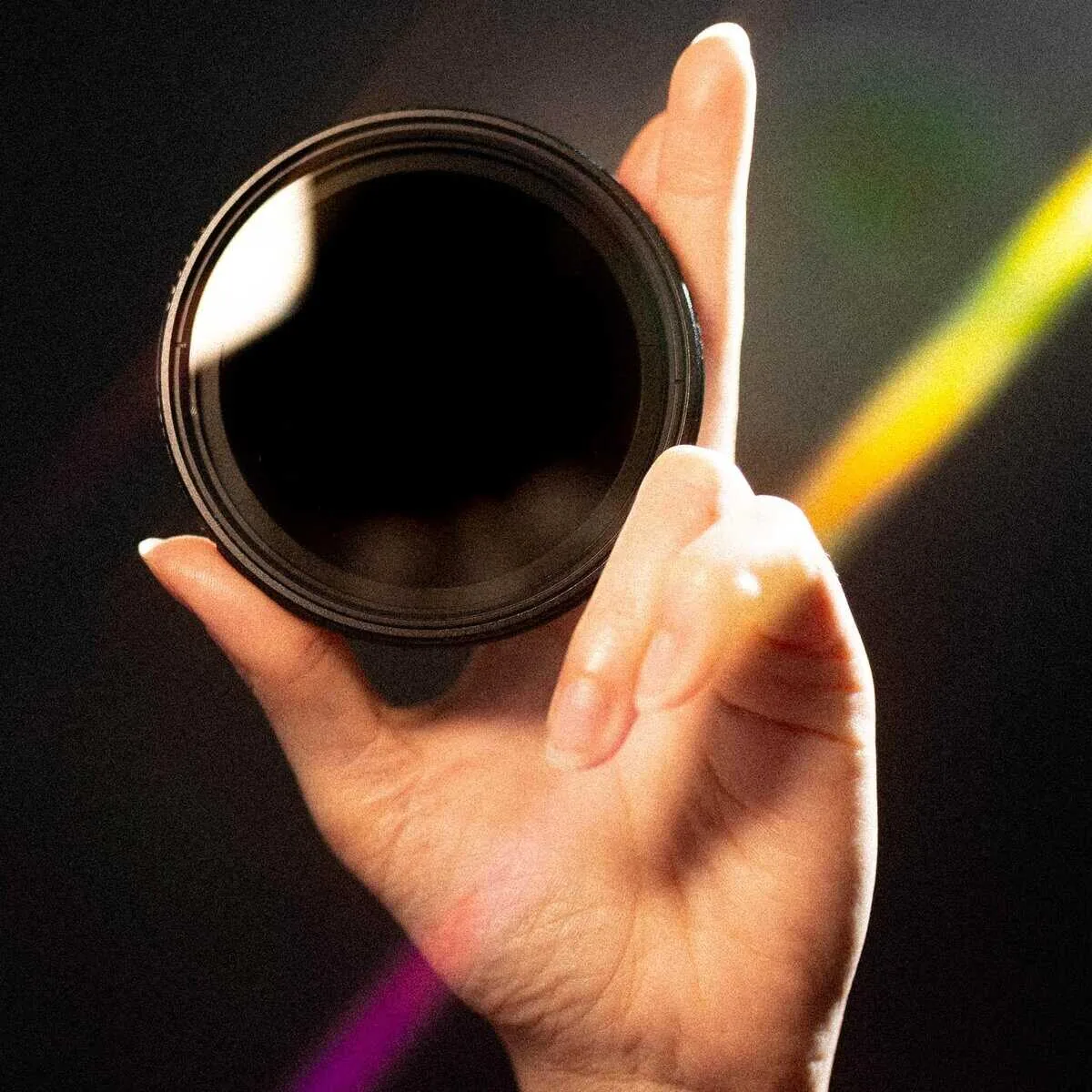 Hand holding an SZ Filters VND with dark glass against a colored background.